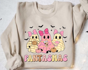 May include: Beige sweatshirt featuring a graphic of three cartoon ghosts with pink bows, holding a pastry, coffee, and a croissant. The word "PANTASMAS" is printed in a retro font below the ghosts. Black bat silhouettes are scattered around the design.