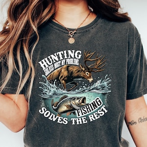 May include: A dark gray t-shirt with a distressed look featuring a graphic of a deer jumping out of the water with a fish. The text on the shirt reads "Hunting solves most my problems Fishing solves the rest".