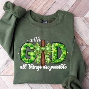 May include: Olive green sweatshirt with the words "with GOD all things are possible." The graphic features a cross and a green bow with shamrock accents. The sweatshirt is made of a soft material.