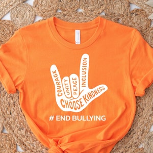 May include: Orange t-shirt with a white hand sign that says "Choose Kindness" with the words "Courage, Unity, Peace, Inclusion" inside the hand sign. The shirt also says "#End Bullying" at the bottom.
