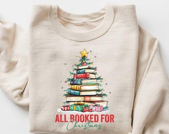 May include: A beige sweatshirt with a Christmas tree made of stacked books and the text "All Booked for Christmas".