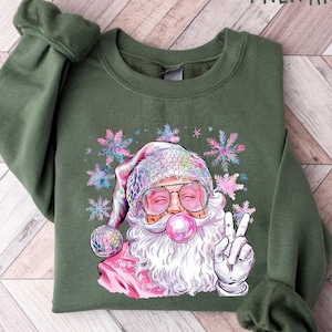 May include: A green sweatshirt with a pink and white Santa Claus graphic. The Santa Claus is wearing sunglasses and blowing a bubble. The graphic also includes snowflakes.