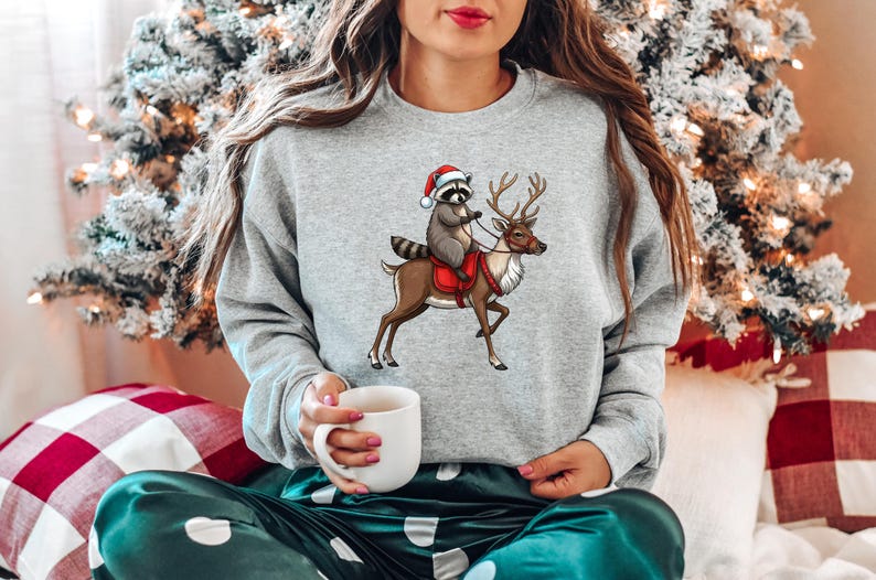 May include: A gray sweatshirt with a Christmas-themed design featuring a raccoon wearing a Santa hat riding a reindeer.