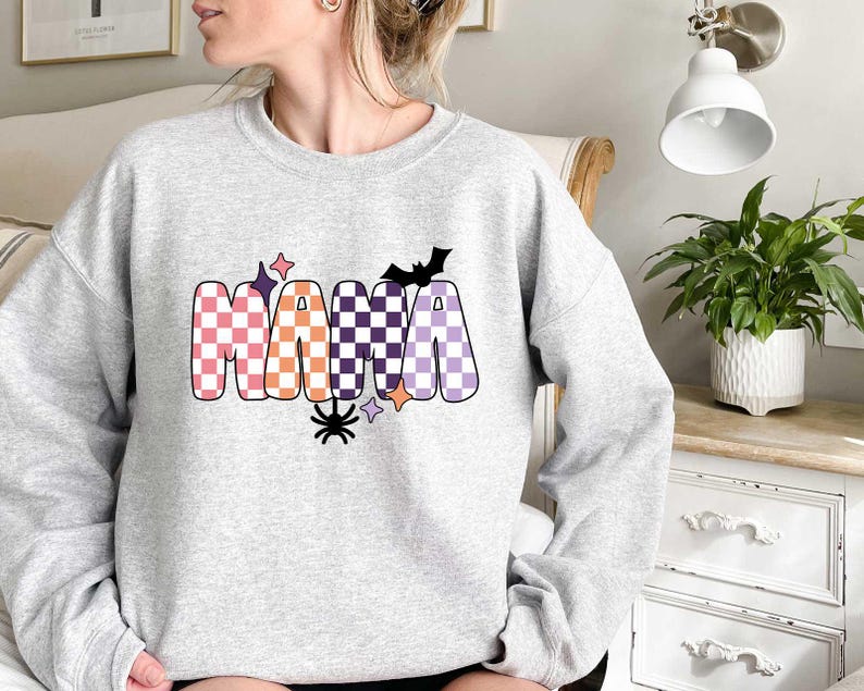 May include: A gray sweatshirt with the word "MAMA" in checkered letters with orange, pink, purple, and black accents. A black bat and spider are also included in the design.