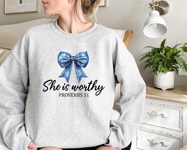 Może przedstawiać: Szara bluza z niebieską wstążką z dżinsu i nadrukiem "She is worthy Proverbs 31" z przodu.