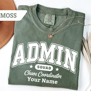 May include: Moss green t-shirt with the word "ADMIN" in large white block letters. Below the word "ADMIN" is the word "SQUAD" with a star, and the words "Chaos Coordinator" and "Your Name". A gold necklace with a pendant is on the shirt.