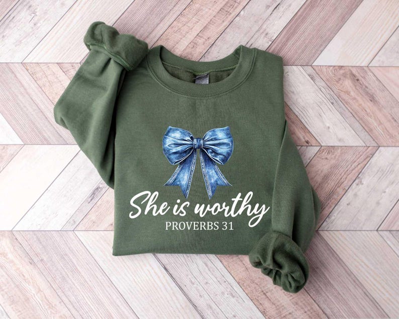 Może przedstawiać: Zielona bluza z niebieską kokardą z dżinsu i nadrukiem "She is worthy Proverbs 31" z przodu.
