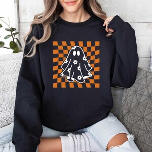 May include: Black sweatshirt featuring a white ghost with a floral pattern on an orange and white chequered background.