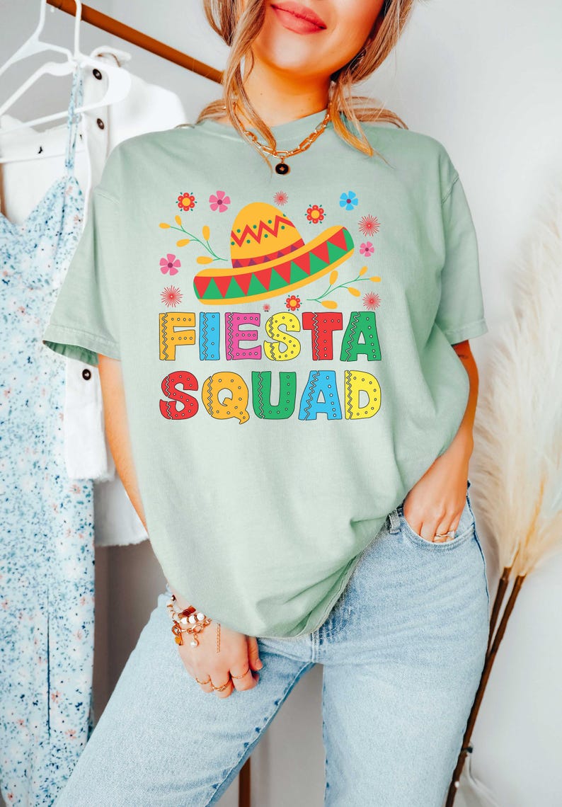 May include: A light green t-shirt with a colorful graphic of a sombrero and flowers. The text "FIESTA SQUAD" is written in colorful letters.