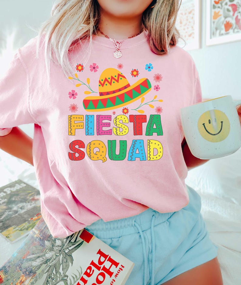 May include: Pink t-shirt with a colorful graphic of a sombrero and the text "Fiesta Squad".