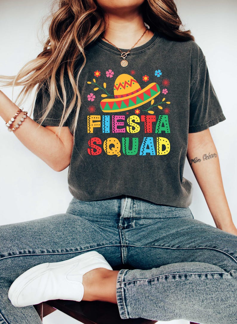 May include: A dark gray t-shirt with a colorful graphic of a sombrero, flowers, and the text "Fiesta Squad".