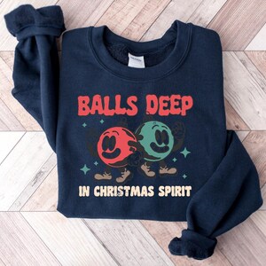 Peut inclure: Un sweat-shirt bleu marine avec le texte "Balls Deep in Christmas Spirit" et un graphique de deux boules de dessin anim&eacute; avec des visages.