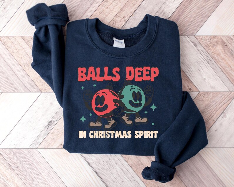 Peut inclure: Un sweat-shirt bleu marine avec le texte "Balls Deep in Christmas Spirit" et un graphique de deux boules de dessin anim&eacute; avec des visages.