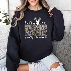 May include: Black sweatshirt with a white deer head and the text "hello hunting season goodbye husband".