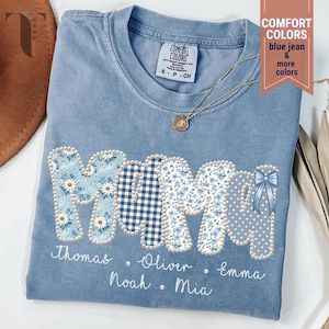 May include: A light blue Comfort Colors t-shirt with the word "MOM" in a patchwork design. The letters are decorated with floral patterns, gingham, and polka dots, outlined with pearls. Names are printed below the letters.