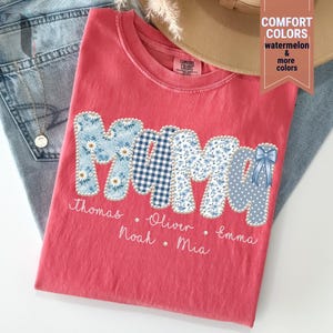 Pu&ograve; includere: Una maglietta color corallo con la scritta "MAMA" in lettere patchwork. Le lettere presentano motivi floreali, a quadretti e a pois. Sotto ci sono i nomi Thomas, Oliver, Noah, Mia ed Emma.
