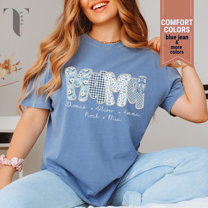 Pu&ograve; includere: Una maglietta blu con la scritta "MOM" in un design patchwork. Le lettere sono decorate con motivi floreali, a quadretti e a pois. Sotto ci sono i nomi Thomas, Oliver, Emma, Noah e Mia. La maglietta ha anche il testo "COMFORT COLORS blue jean & more colors".
