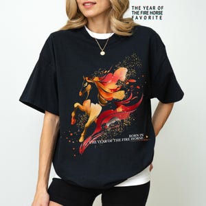 Pu&ograve; includere: T-shirt nero con un'illustrazione ad acquerello di un cavallo nei toni del rosso e dell'arancione. La maglietta presenta il testo "THE YEAR OF THE FIRE HORSE FAVORITE" e "BORN IN THE YEAR OF THE FIRE HORSE".