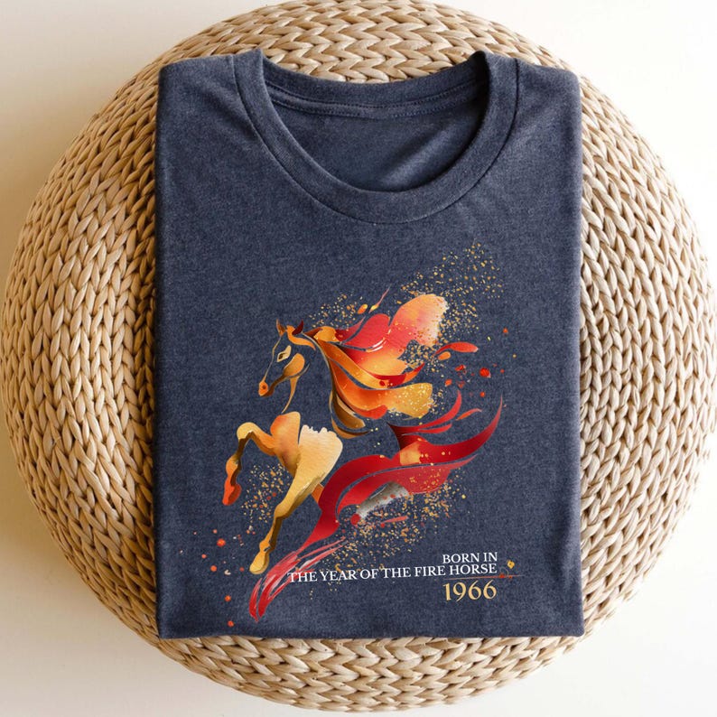Pu&ograve; includere: T-shirt blu navy con un'illustrazione stilizzata di un cavallo nei toni dell'arancione, rosso e oro. Il testo "BORN IN THE YEAR OF THE FIRE HORSE 1966" &egrave; stampato sotto. Il cavallo ha una criniera e una coda fluenti.