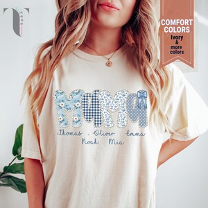 Pu&ograve; includere: T-shirt color crema con la scritta "MOM" in motivi floreali, a quadri e a pois blu. I nomi Thomas, Oliver, Emma, Noah e Mia sono stampati sotto. La maglietta presenta anche un fiocco.