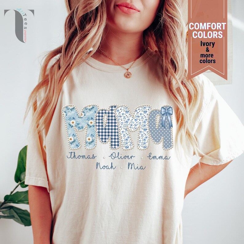Pu&ograve; includere: T-shirt color crema con la scritta "MOM" in motivi floreali, a quadri e a pois blu. I nomi Thomas, Oliver, Emma, Noah e Mia sono stampati sotto. La maglietta presenta anche un fiocco.