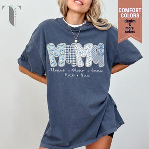 Pu&ograve; includere: T-shirt blu scuro con la scritta "MOM" in lettere patchwork. Ogni lettera presenta un motivo blu diverso, tra cui floreale, quadretti e pois. Sotto le lettere sono stampati i nomi Thomas, Oliver, Emma, Noah e Mia.