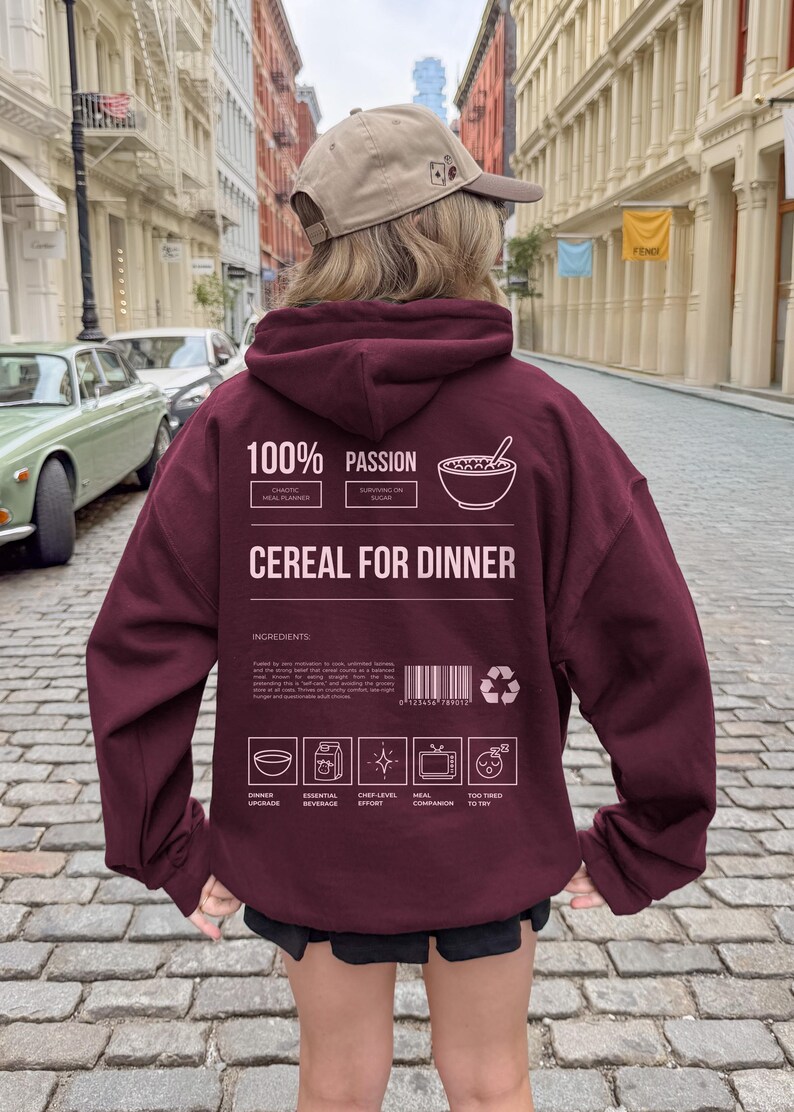 Może przedstawiać: Bordowa bluza z kapturem z napisem "CEREAL FOR DINNER" i elementami graficznymi. Tył bluzy z kapturem zawiera słowa "100% PASSION" i "INGREDIENTS". Osoba ma na sobie beżową czapkę z daszkiem.