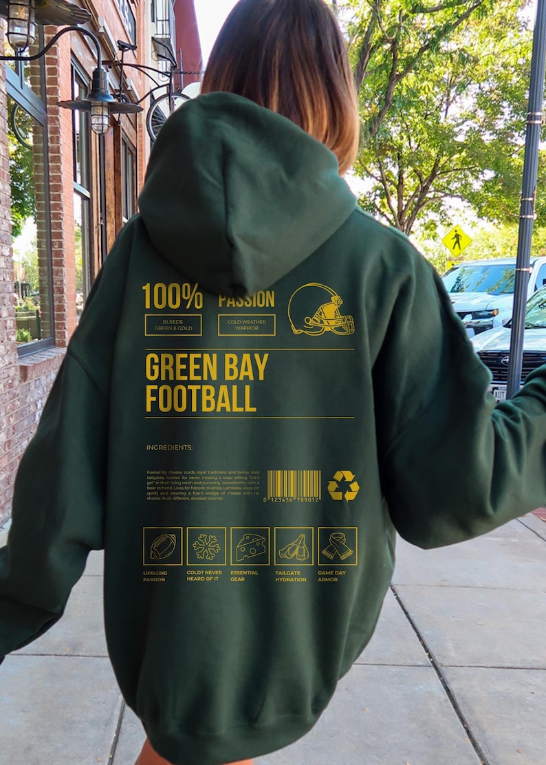 May include: Dark green hoodie with gold text and graphics. The back of the hoodie features the words "GREEN BAY FOOTBALL" and "100% PASSION". Additional text includes "BLEEDS GREEN & COLD" and "COLD WEATHER WARRIOR".