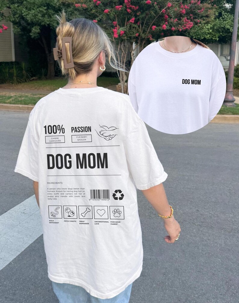 May include: White t-shirt with a graphic print on the back that says "100% Passion" and "Dog Mom". The graphic includes a dog paw print and a heart. The front of the shirt has the text "Dog Mom" printed on it.