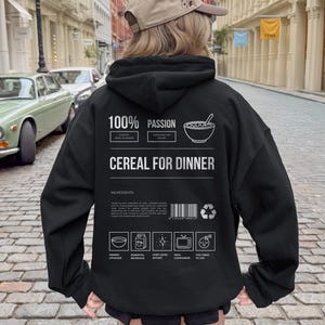 Może przedstawiać: Czarna bluza z kapturem z napisem "100% PASSION" i "CEREAL FOR DINNER". Tył bluzy z kapturem przedstawia grafikę miski płatk&oacute;w śniadaniowych i łyżki. Dodatkowy tekst zawiera "CHAOTIC MEAL PLANNER" i "SURVIVING ON SUGAR".