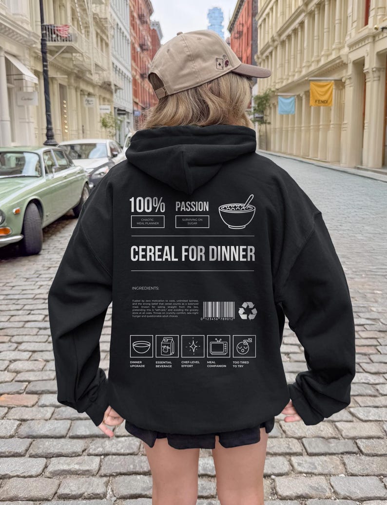 Może przedstawiać: Czarna bluza z kapturem z napisem "100% PASSION" i "CEREAL FOR DINNER". Tył bluzy z kapturem przedstawia grafikę miski płatk&oacute;w śniadaniowych i łyżki. Dodatkowy tekst zawiera "CHAOTIC MEAL PLANNER" i "SURVIVING ON SUGAR".