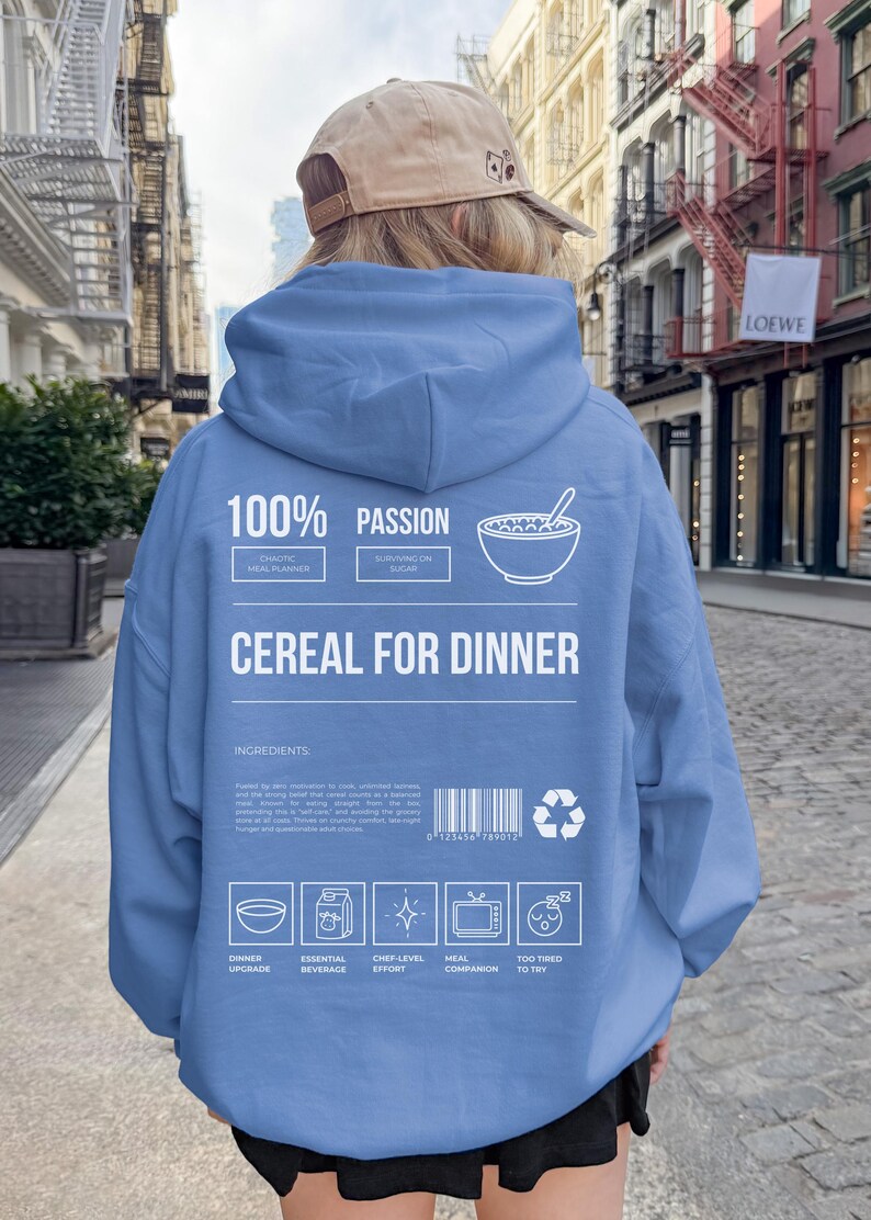 Może przedstawiać: Jasnoniebieska bluza z kapturem z białym napisem "CEREAL FOR DINNER". Tył bluzy z kapturem zawiera r&oacute;wnież słowa "100% PASSION" i r&oacute;żne ikony. Osoba ma na sobie beżową czapkę z daszkiem.
