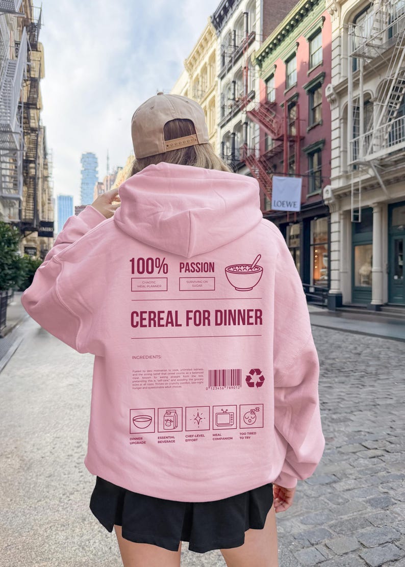 Może przedstawiać: Jasnor&oacute;żowa bluza z kapturem z napisem "100% Passion Cereal for Dinner" z tyłu. Bluza ma kaptur i długie rękawy. Tło przedstawia ulicę miasta z budynkami.