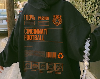 May include: Black hoodie with orange text and graphics. The text reads "100% Passion" and "Cincinnati Football." A tiger graphic is also present. Additional text includes "Game Day Ritual" and "Spicy Fuel."