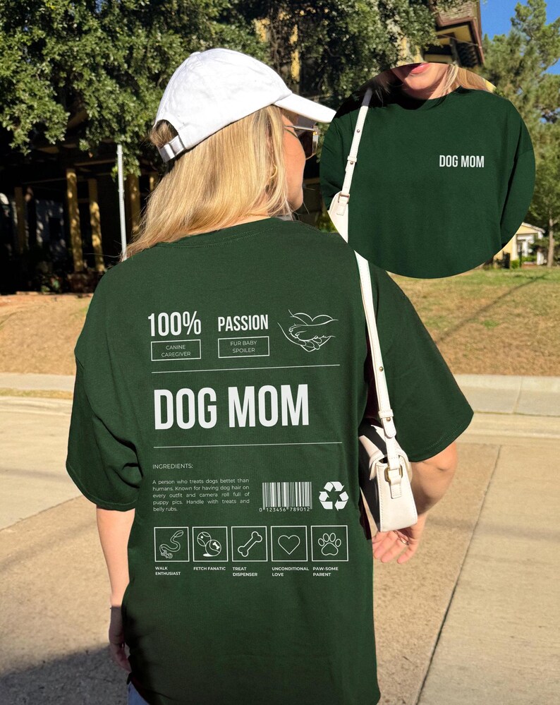 May include: Green t-shirt with white text that reads "100% Passion Canine Caregiver Fur Baby Spoiler Dog Mom". The shirt also has a graphic of a hand holding a paw. The text "Ingredients" is followed by a description of a dog mom. The shirt also has a barcode and recycling symbol. Below the description are five icons: Walk Enthusiast, Fetch Fanatic, Treat Dispenser, Unconditional Love, Paw-some Parent.