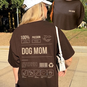 May include: Brown t-shirt with the text "DOG MOM" printed on the front and a graphic on the back that says "100% Passion" with a list of ingredients for being a dog mom, including "Walk Enthusiast", "Fetch Fanatic", "Treat Dispenser", "Unconditional Love", and "Raw Some Parent".