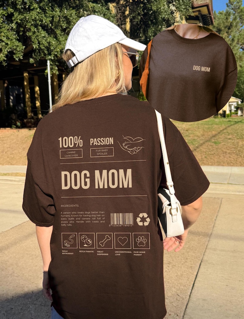 May include: Brown t-shirt with the text "DOG MOM" printed on the front and a graphic on the back that says "100% Passion" with a list of ingredients for being a dog mom, including "Walk Enthusiast", "Fetch Fanatic", "Treat Dispenser", "Unconditional Love", and "Raw Some Parent".