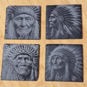 Puede incluir: Cuatro posavasos cuadrados de pizarra con retratos grabados de un jefe nativo americano. Los posavasos grises muestran representaciones detalladas de la cara y el tocado del jefe. Están dispuestos sobre una superficie de madera de color marrón claro.