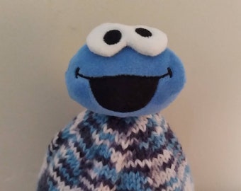 May include: A blue and white knitted hat with a blue plush Cookie Monster character on top.