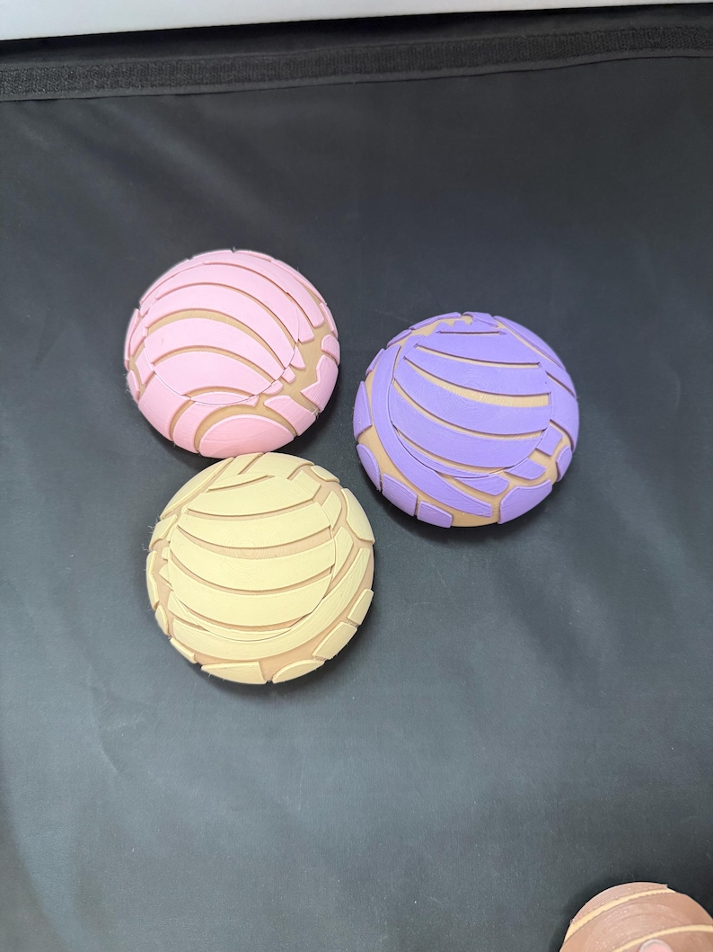 May include: Three colourful, round, decorative items with a unique design. The items are pink, purple, and yellow with a pattern of lines and curves.
