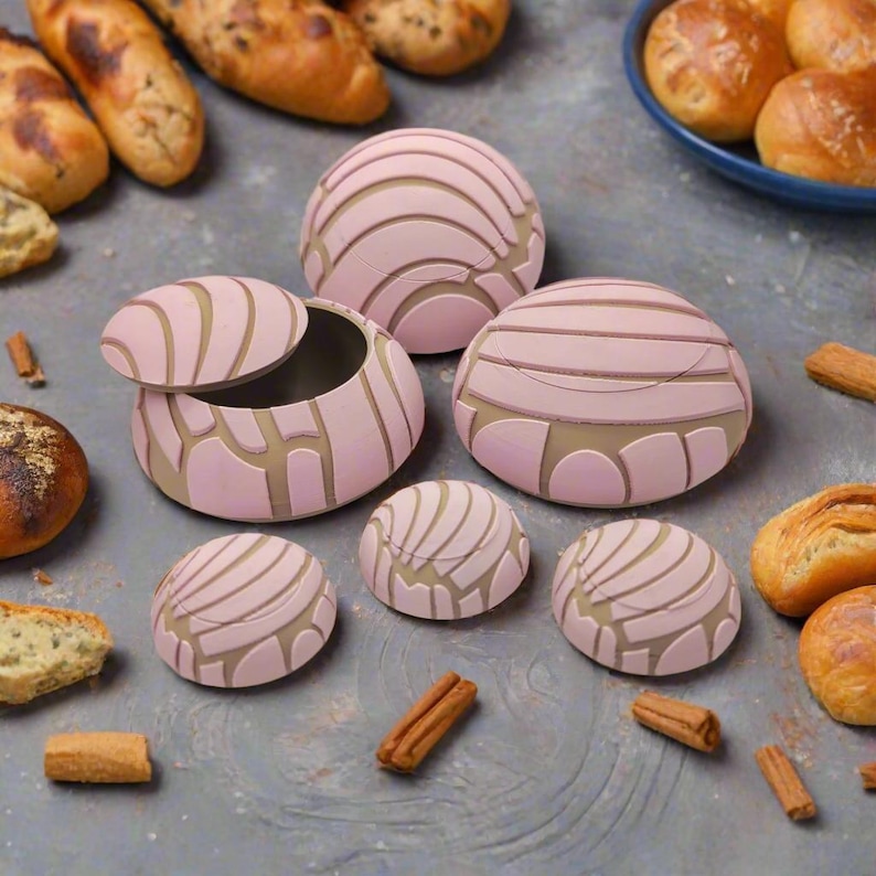 May include: A set of six pink and white concha-shaped containers, some with lids, on a grey surface with cinnamon sticks.