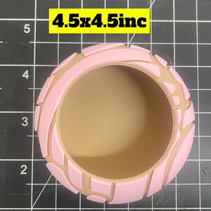 May include: A pink and brown concha, a type of Mexican sweet bread, with a decorative design. The concha is 4.5 inches by 4.5 inches.