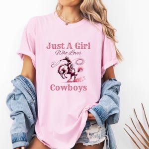 May include: Pink t-shirt with the text "Just A Girl Who Loves Cowboys" and a graphic of a woman riding a horse.