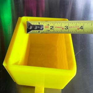 May include: A bright yellow plastic tray with a small handle on the bottom. The tray is 2 inches wide and 3 inches long. The tray is made of a durable plastic and is perfect for holding small items.