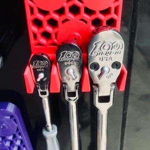 May include: A red tool holder with three chrome ratchets. The ratchets have the text "100 Snap-on USA" on them. The tool holder has the text "StoreSZY" on it.