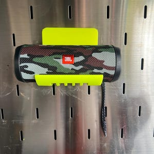 May include: A bright yellow speaker holder with a camo-patterned JBL portable speaker attached. The holder has a small black cord hanging from it.