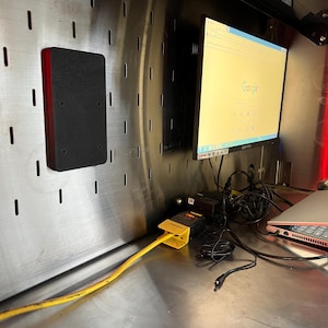 Peut inclure: Gros plan sur un espace de travail avec un ordinateur portable, un moniteur affichant la page d'accueil de Google et une rallonge jaune. Le moniteur est monté sur un mur avec un panneau perforé noir.