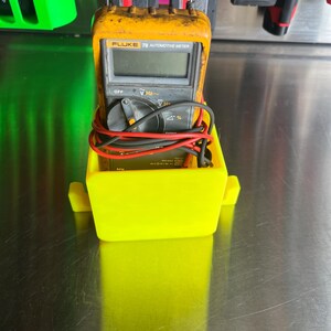 May include: A yellow plastic holder with a black and yellow Fluke 78 Automotive Meter inside. The meter has a digital display and a red knob.