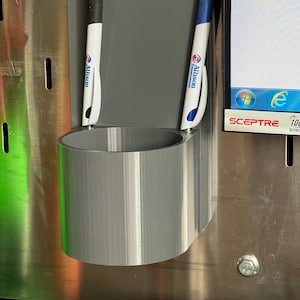 Könnte beinhalten: Ein grauer Plastik-Stiftbehälter mit zwei Stiften darin. Die Stifte sind weiß mit blauen Akzenten und haben das Logo "Allison Transmission" aufgedruckt.