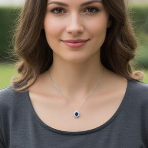 May include: A silver necklace with a pendant featuring a dark blue oval gemstone surrounded by small white gemstones. The necklace is worn against a gray top.
